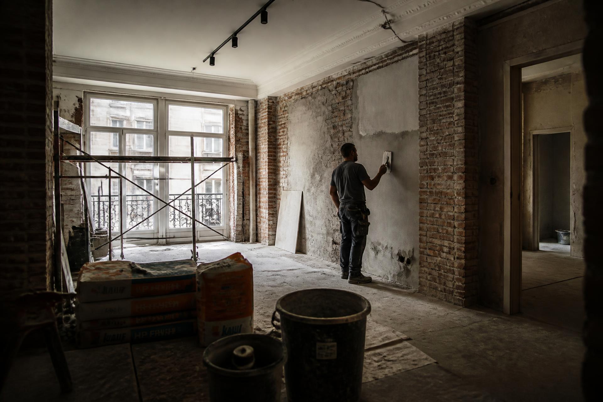 Reforma de apartamento em andamento, com profissional aplicando reboco na parede